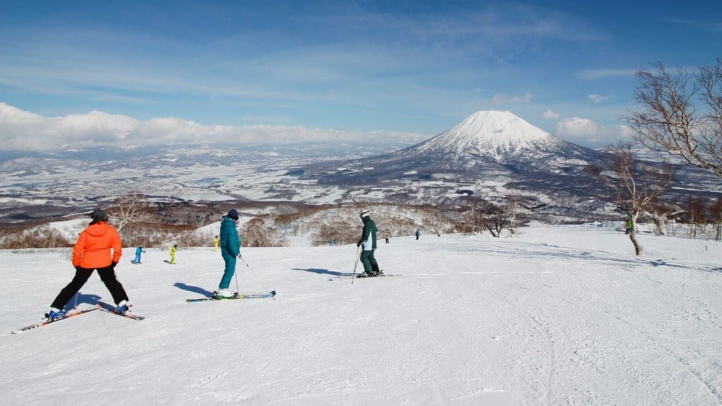Skiers pause on a wide groomed run at Grand Hirafu with Mt. Yotei rising across the valley