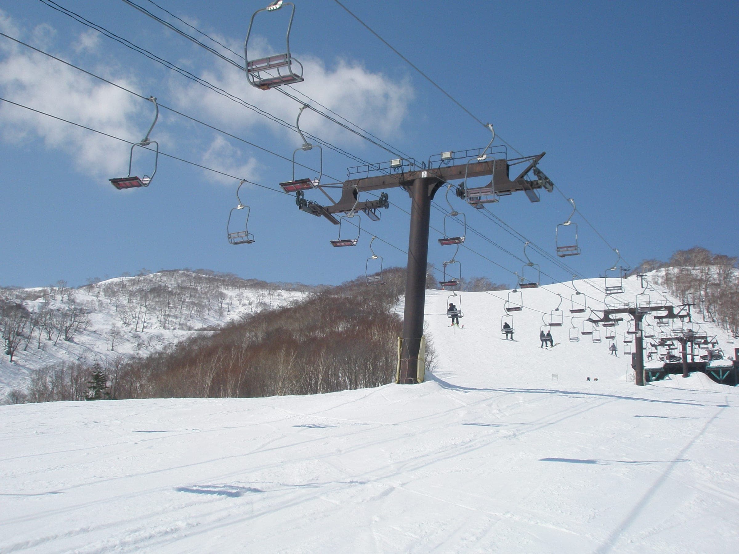 Two pair lifts share one line of towers on a sunny slope at Grand Hirafu