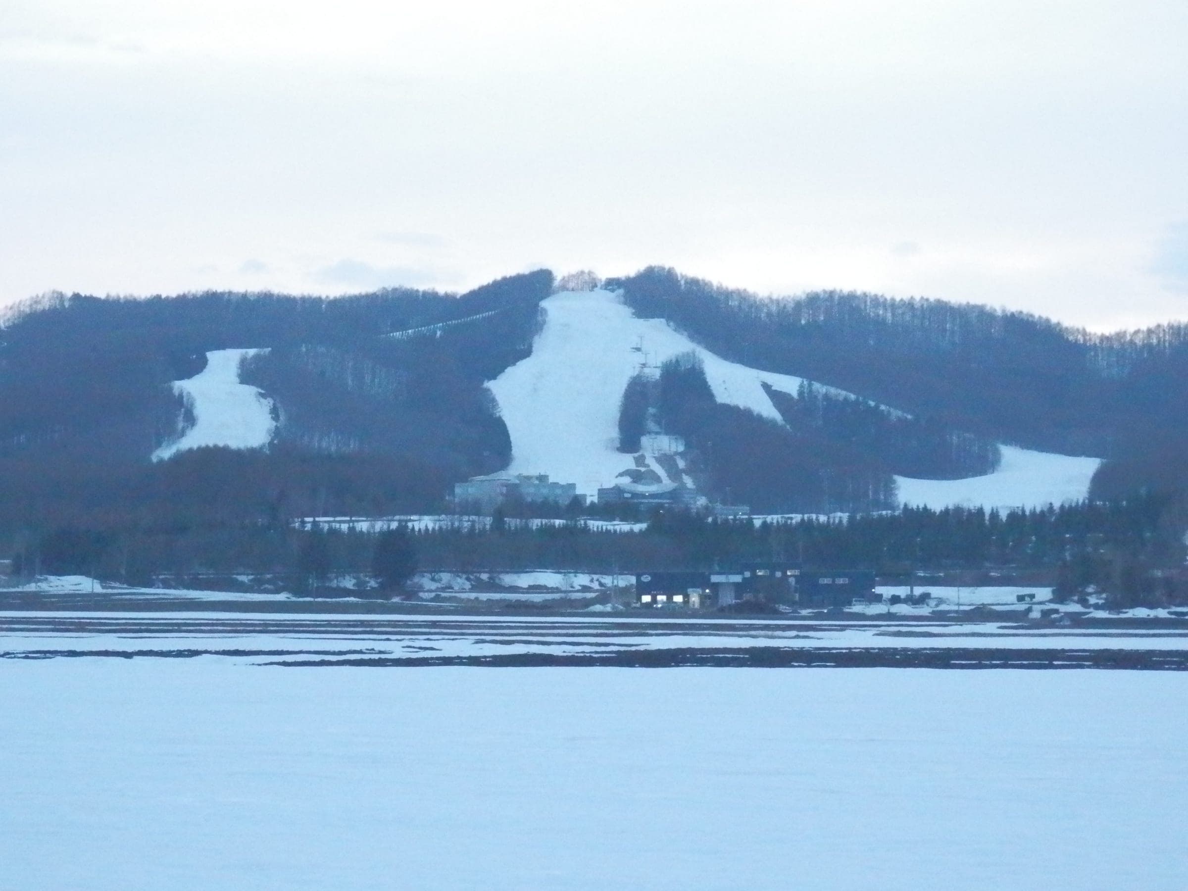 The open runs of Northern Arc Resort cut white bands through a forested hill above snowy fields