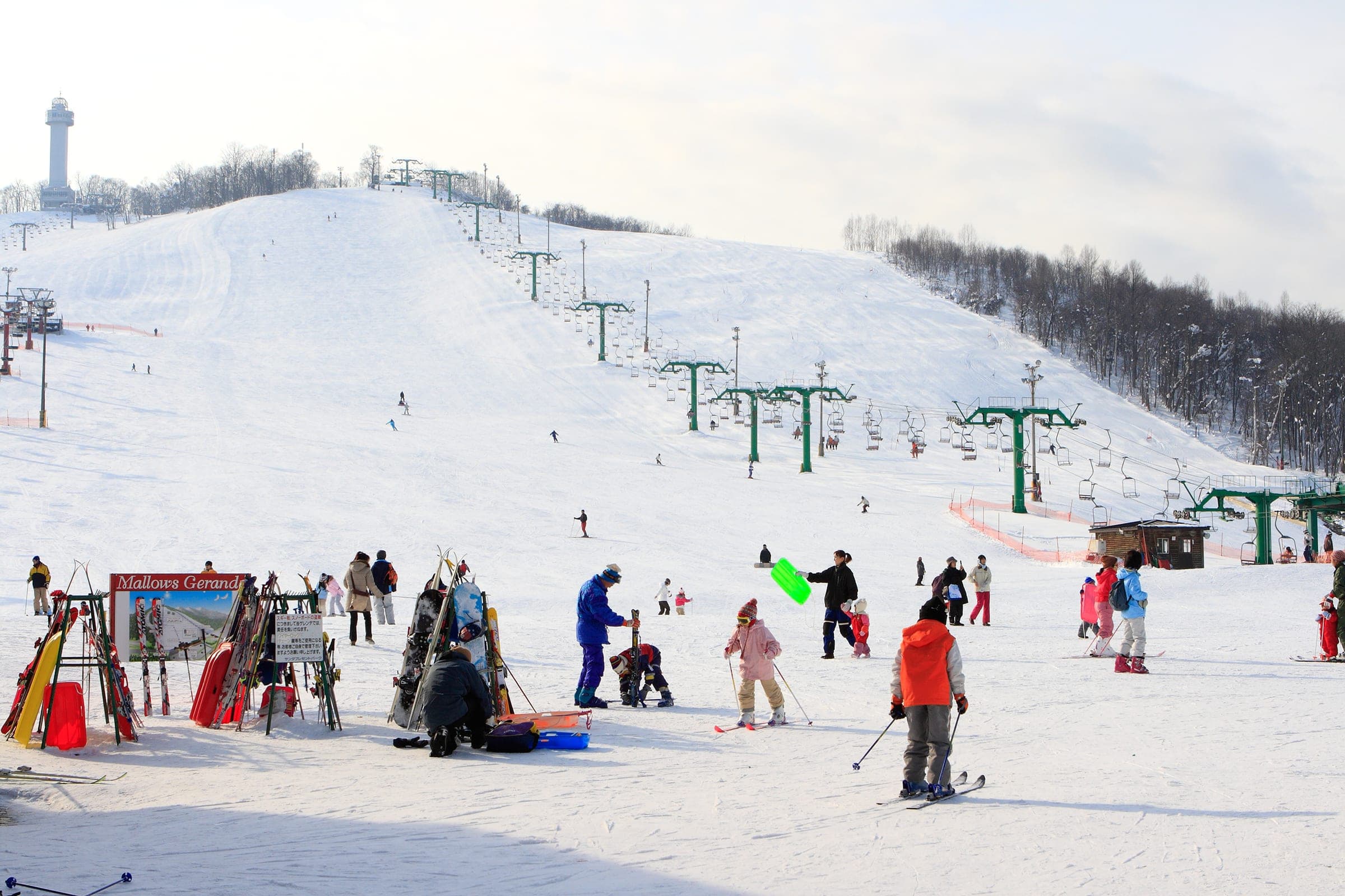 Skiers and sledders fill the gentle slope below the lifts at Santa Present Park in Asahikawa