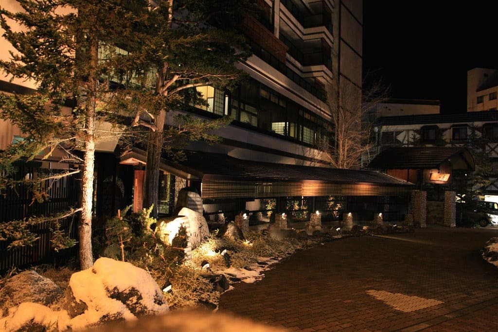 Lanterns light snow-covered rocks along the entrance drive of Akan Tsuruga Besso Hinanoza at night