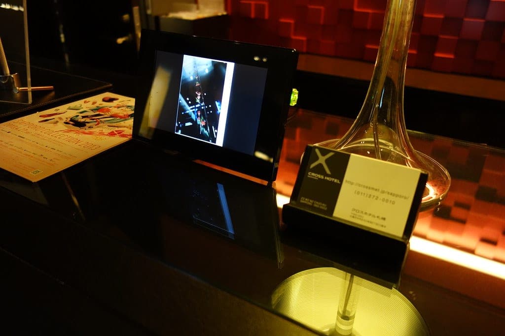 A desk at Cross Hotel Sapporo holds a digital photo frame, a glass carafe and an X-branded card