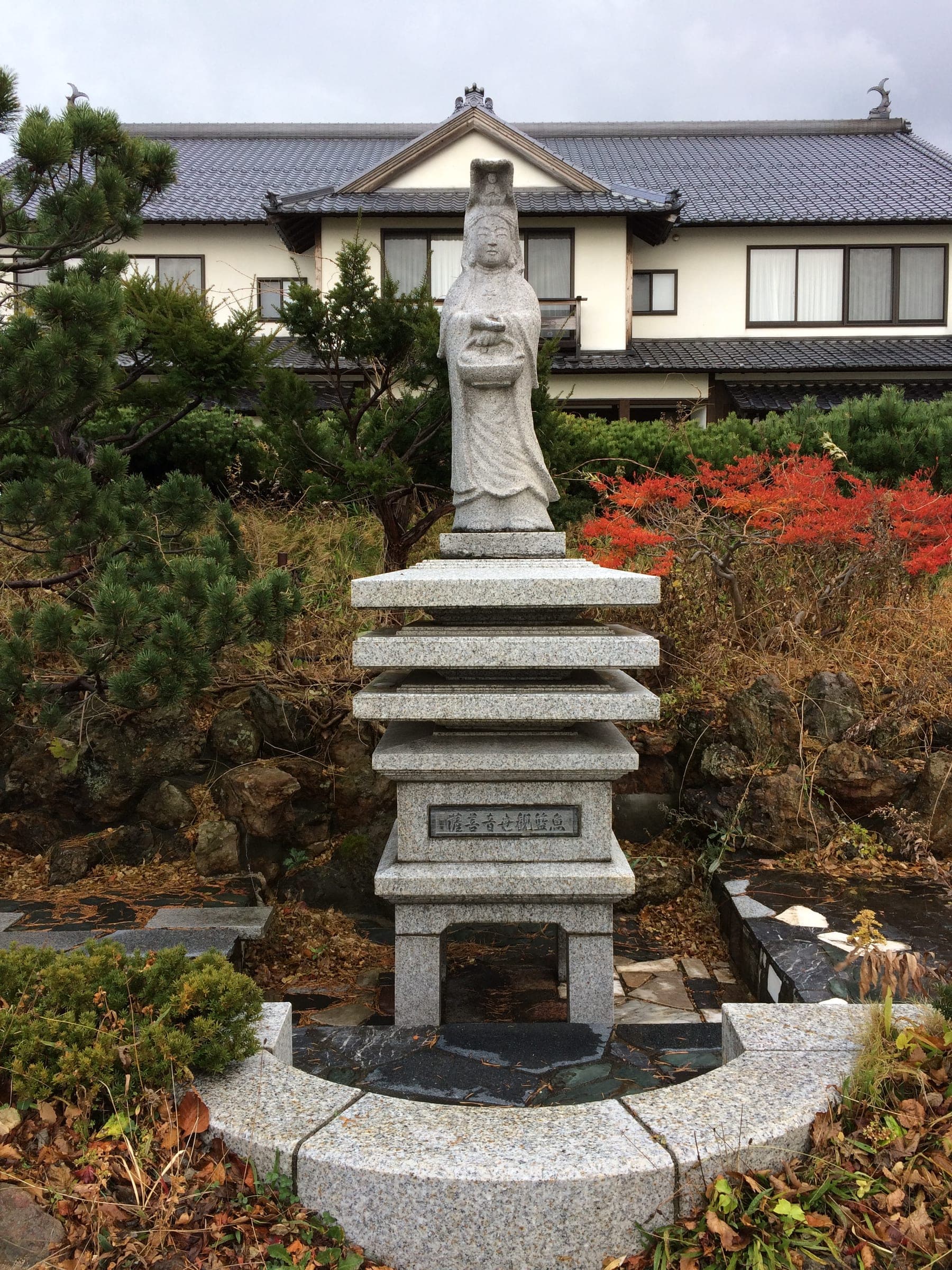 A stone Kannon statue in the gardens of Ginrinsou with red leaves behind