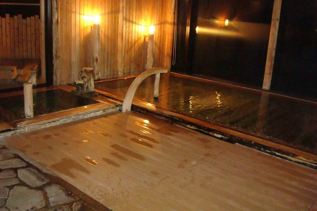 Wall lamps light the timber-lined indoor bath at La Vista Daisetsuzan beside a dark window