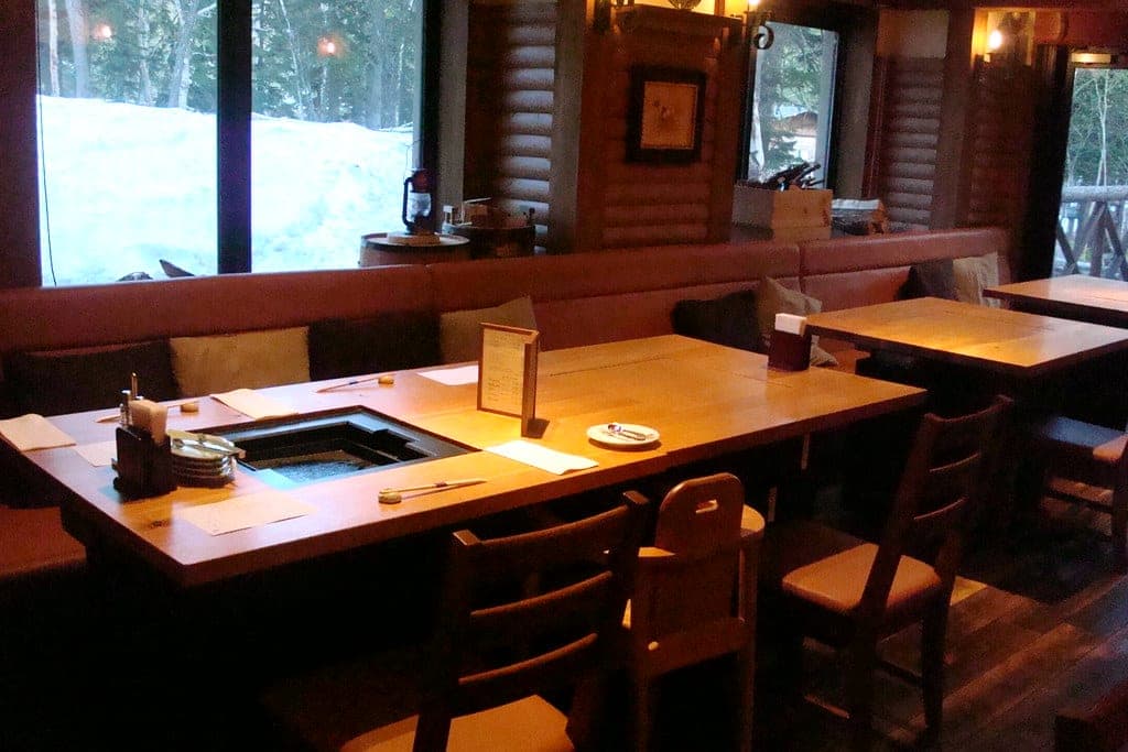 La Vista Daisetsuzan's dining room with grill tables and windows onto the snowy forest