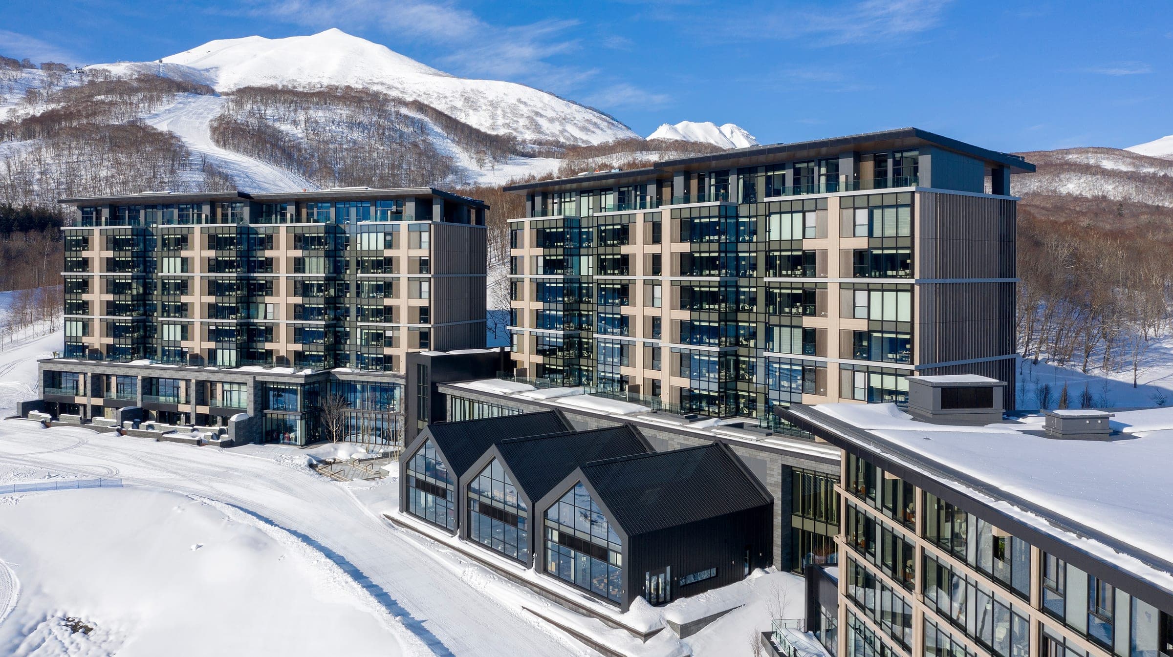 Park Hyatt Niseko Hanazono's timber and glass wings in snow below the slopes of Niseko Annupuri
