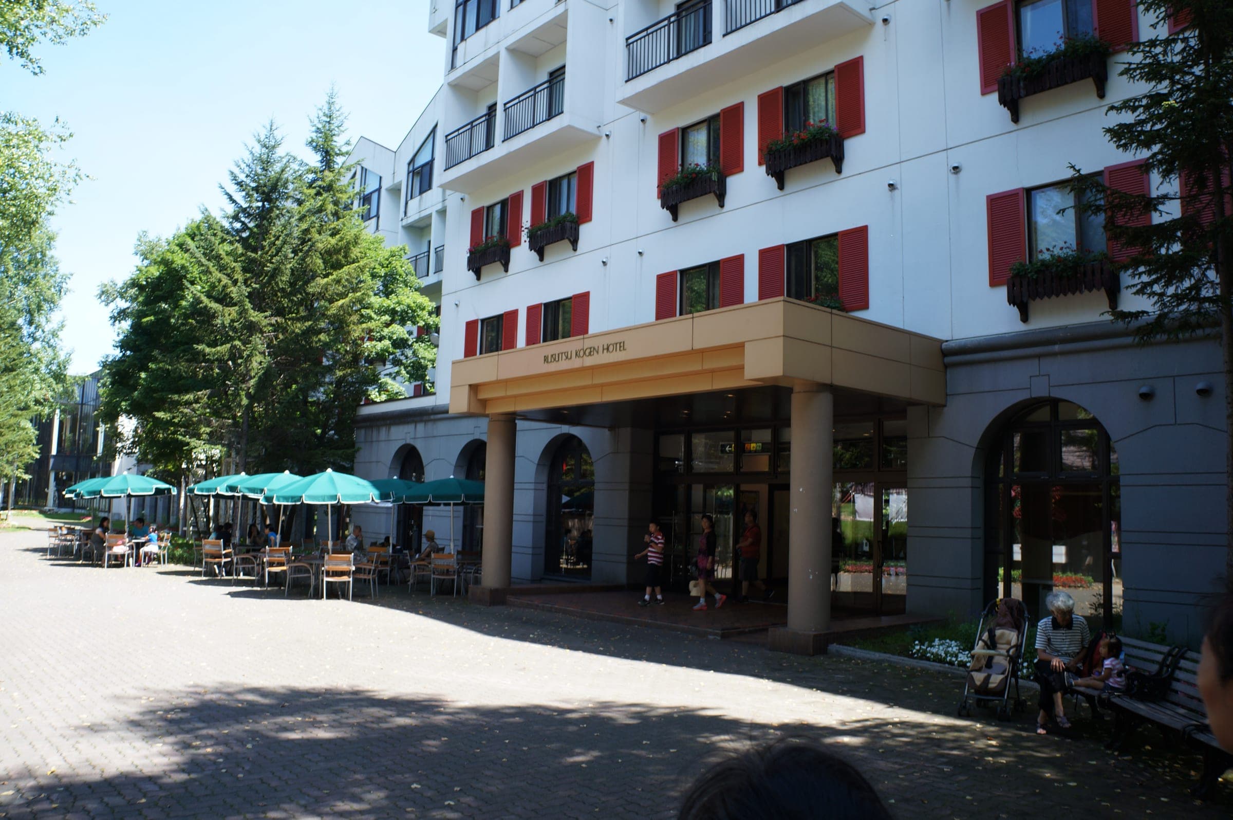 Rusutsu Resort Hotel's white facade with red shutters and a café terrace in summer