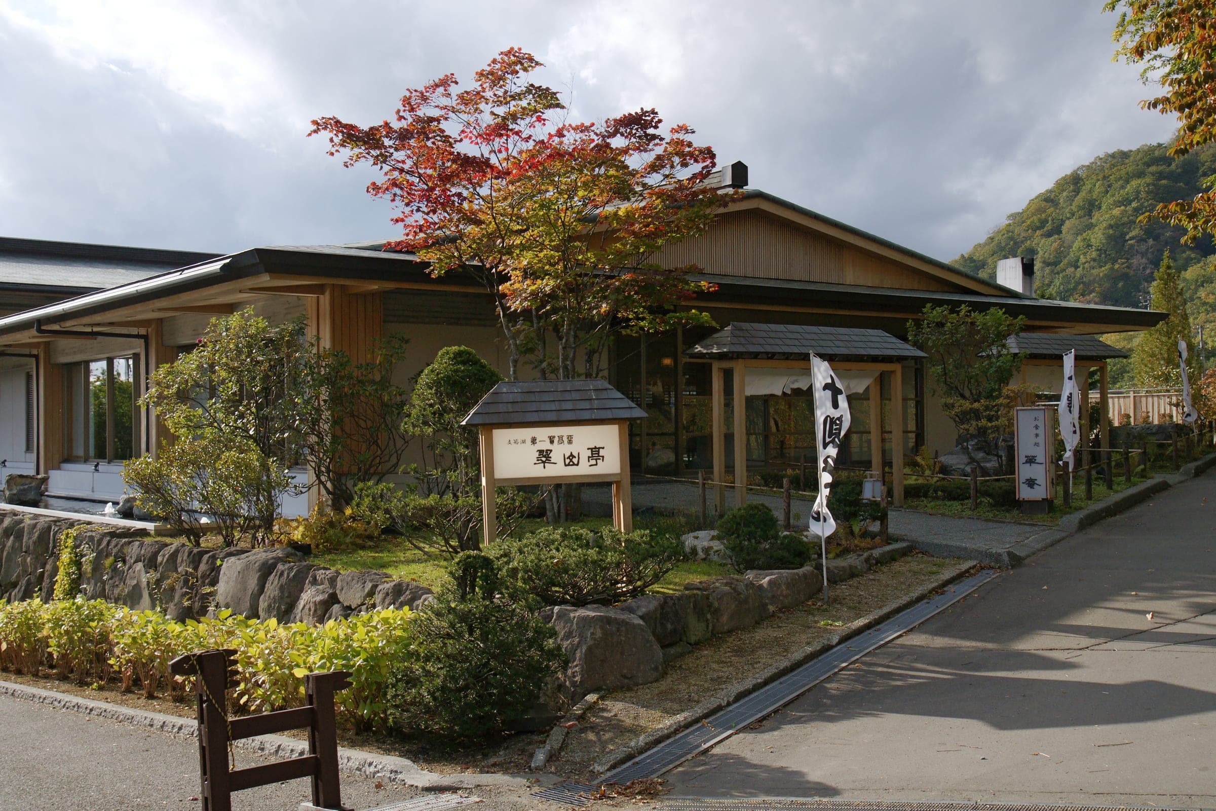 Autumn maples and a timber signboard stand before the low wooden wing of Suizantei at Shikotsuko Onsen