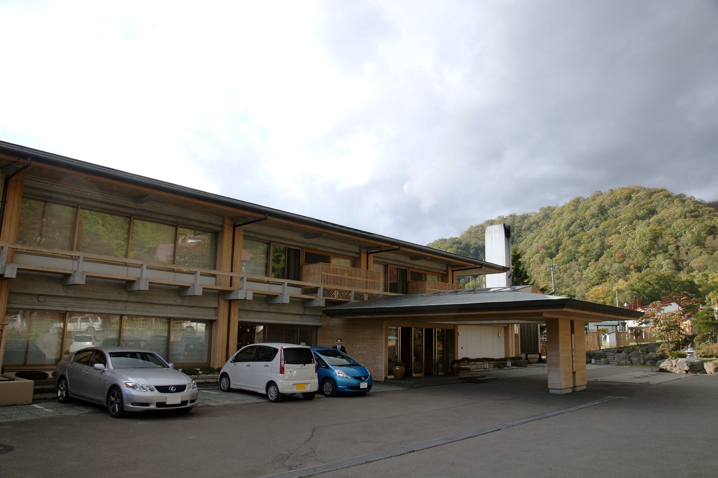 Suizantei's two-storey timber front and covered drive-up entrance below a wooded hill at Lake Shikotsu
