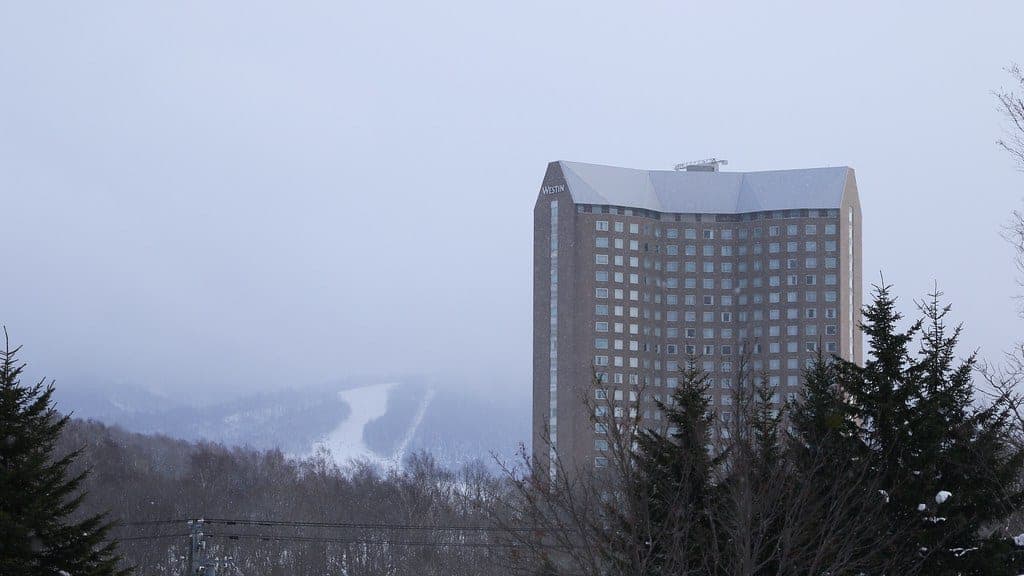 The Westin Rusutsu tower stands above snowy forest with the Rusutsu ski runs behind