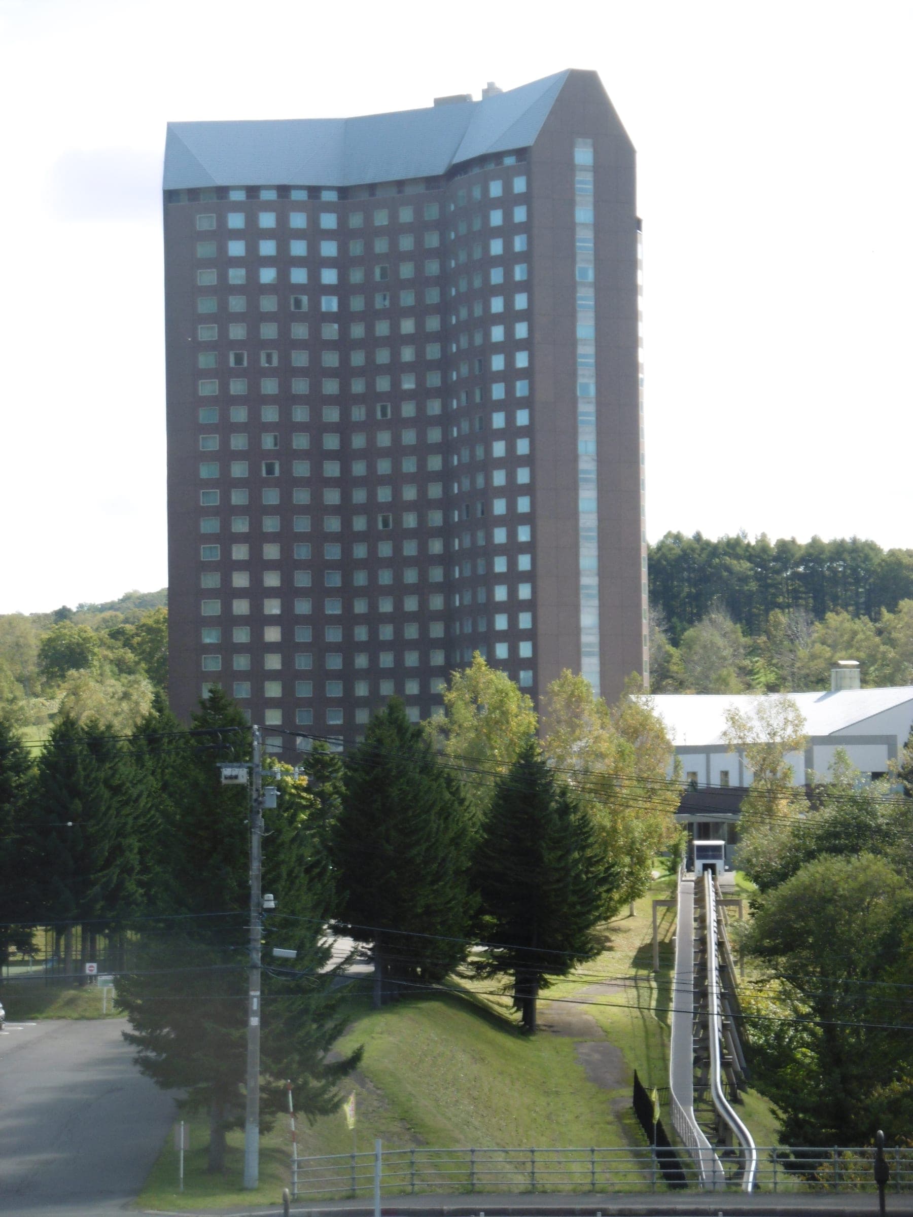 The Westin Rusutsu tower rises over trees and the low resort buildings on a summer day