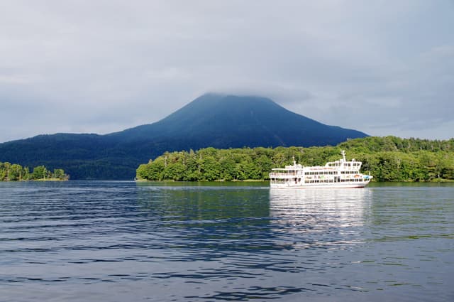 Mt. Oakan rises over Lake Akan as a sightseeing boat passes a wooded island