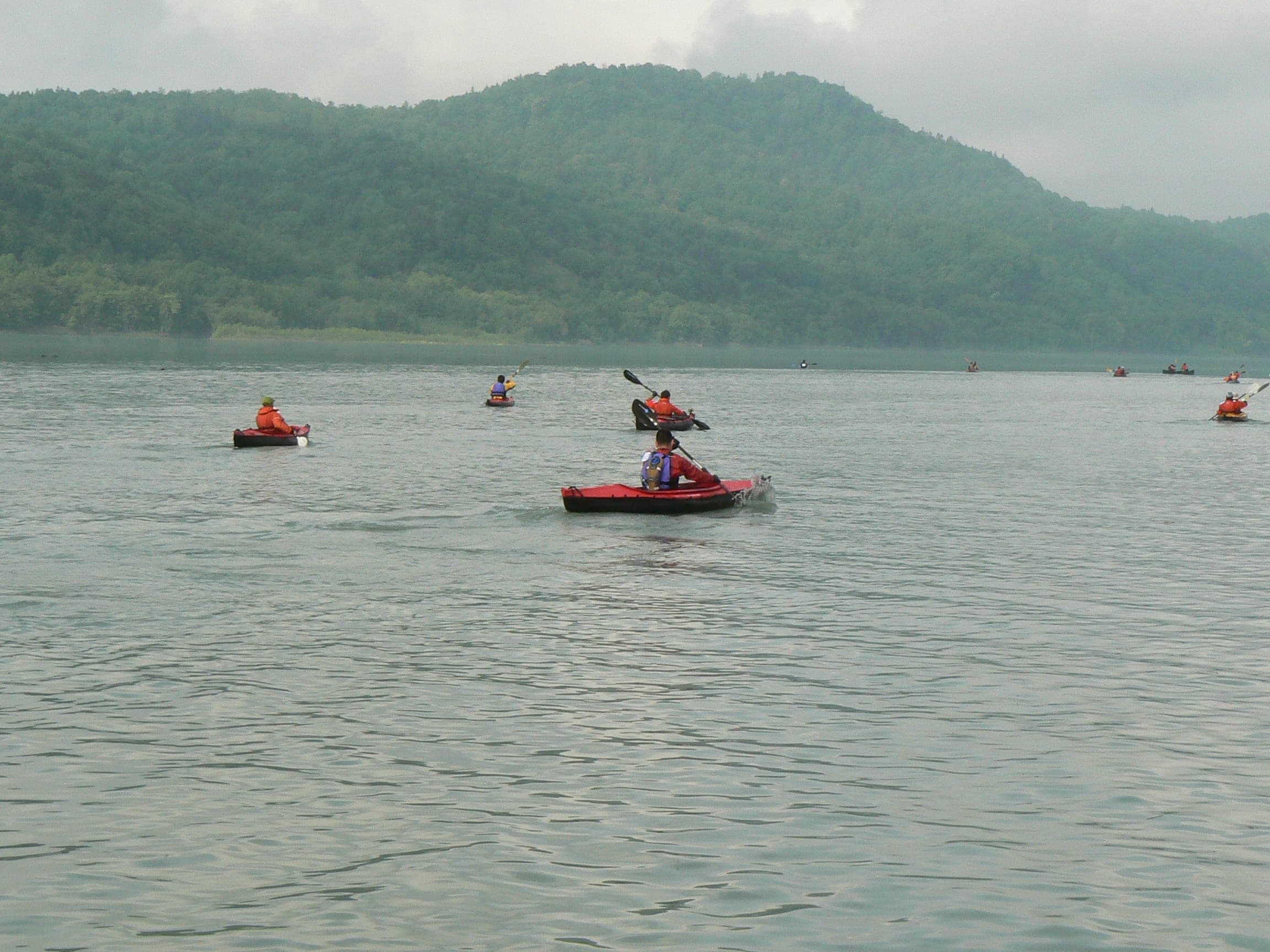 Kayakers paddle across Chubetsu Reservoir below forested hills in Higashikawa