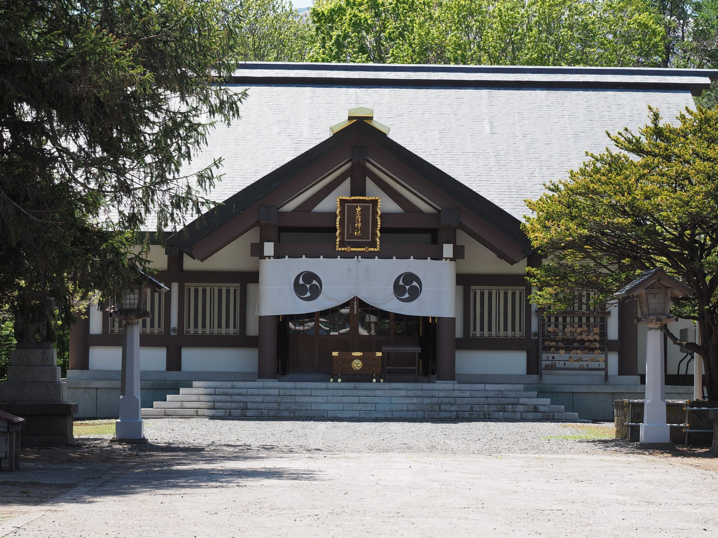 The main hall of Iwanai Shrine, with a white curtain across its entrance and trees on either side