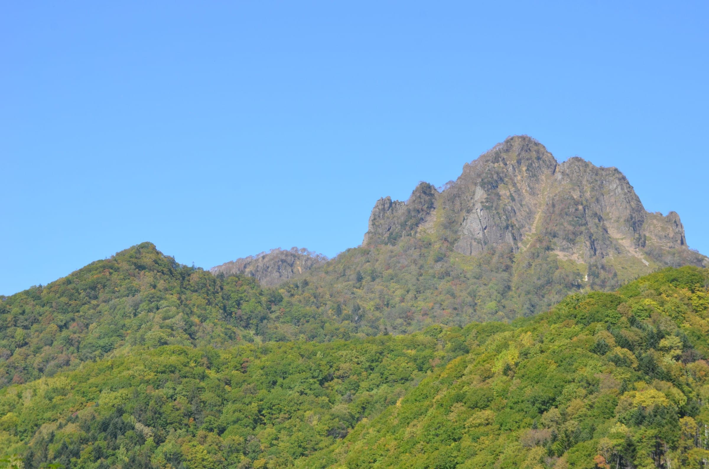 The jagged summit of Mount Tengu rises over green forest above Jozankei