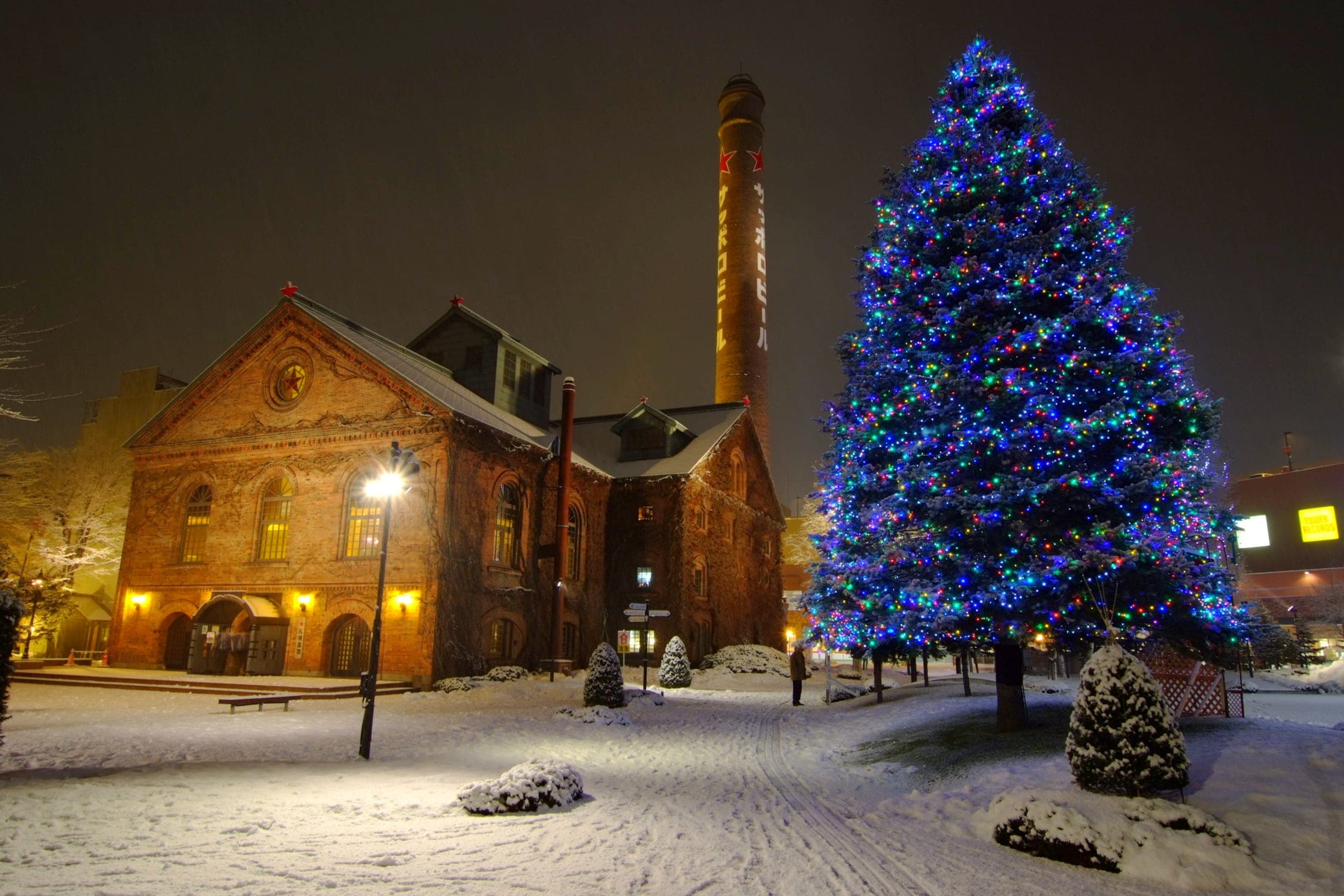 The red-brick halls of the Sapporo Beer Garden complex at night with a lit tree in the snow