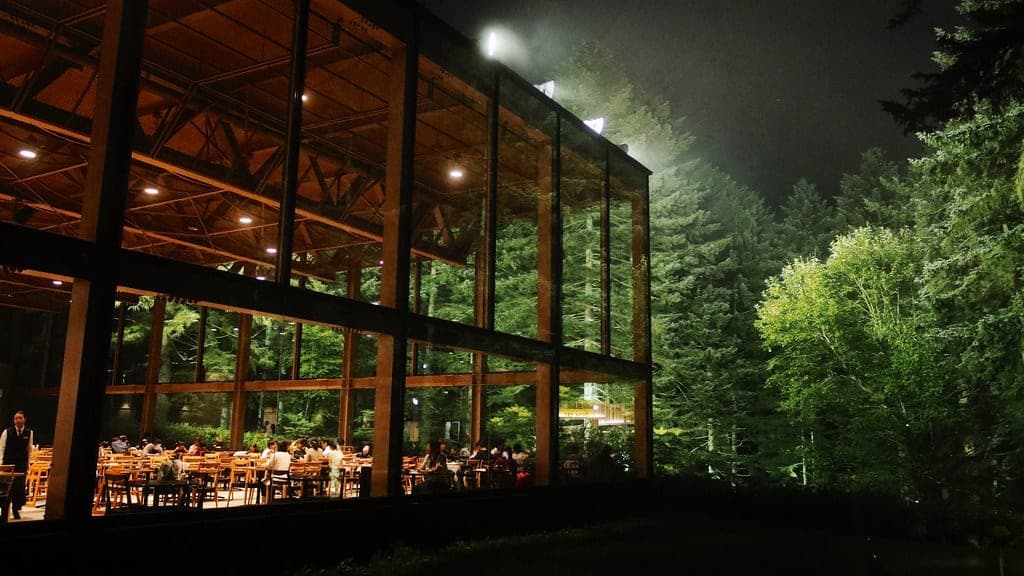 The glass dining hall of Nininupuri glows among dark forest at Tomamu at night