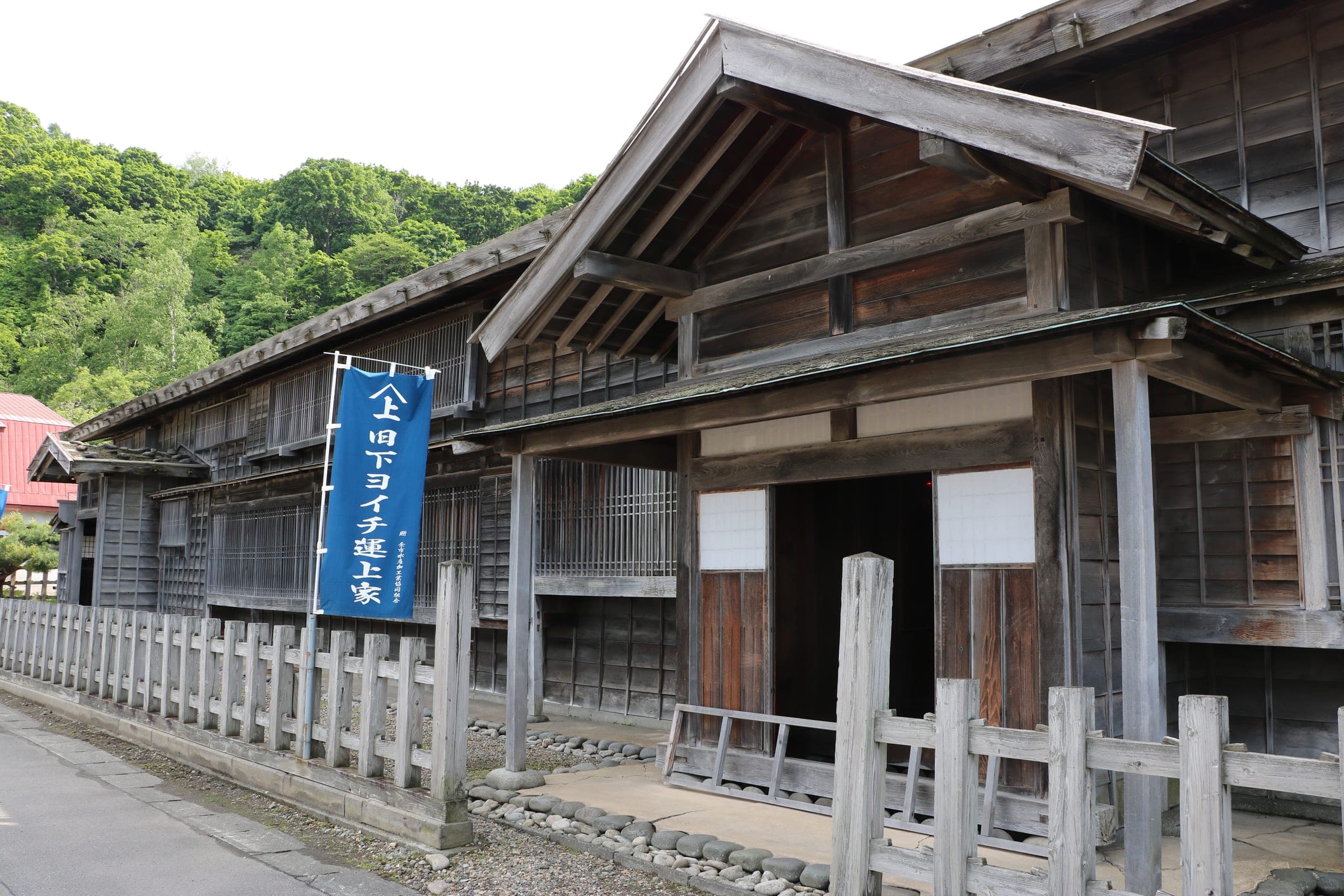 The weathered timber Former Shimo-Yoichi Unjoya trading post behind a wooden fence