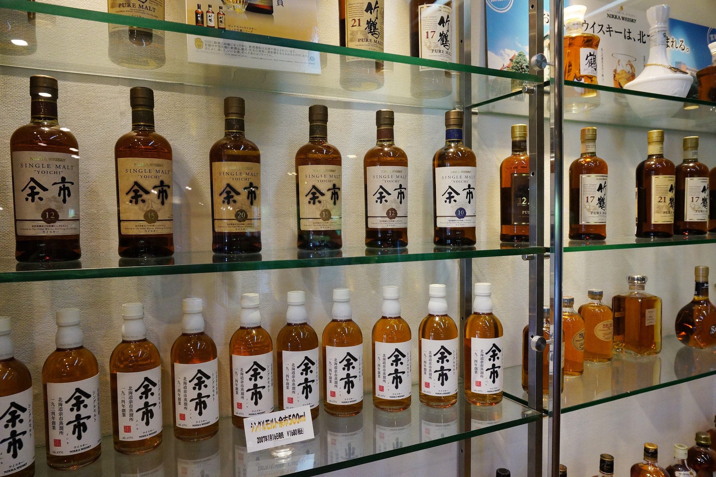 Rows of Nikka whisky bottles on glass shelves at the Yoichi Distillery