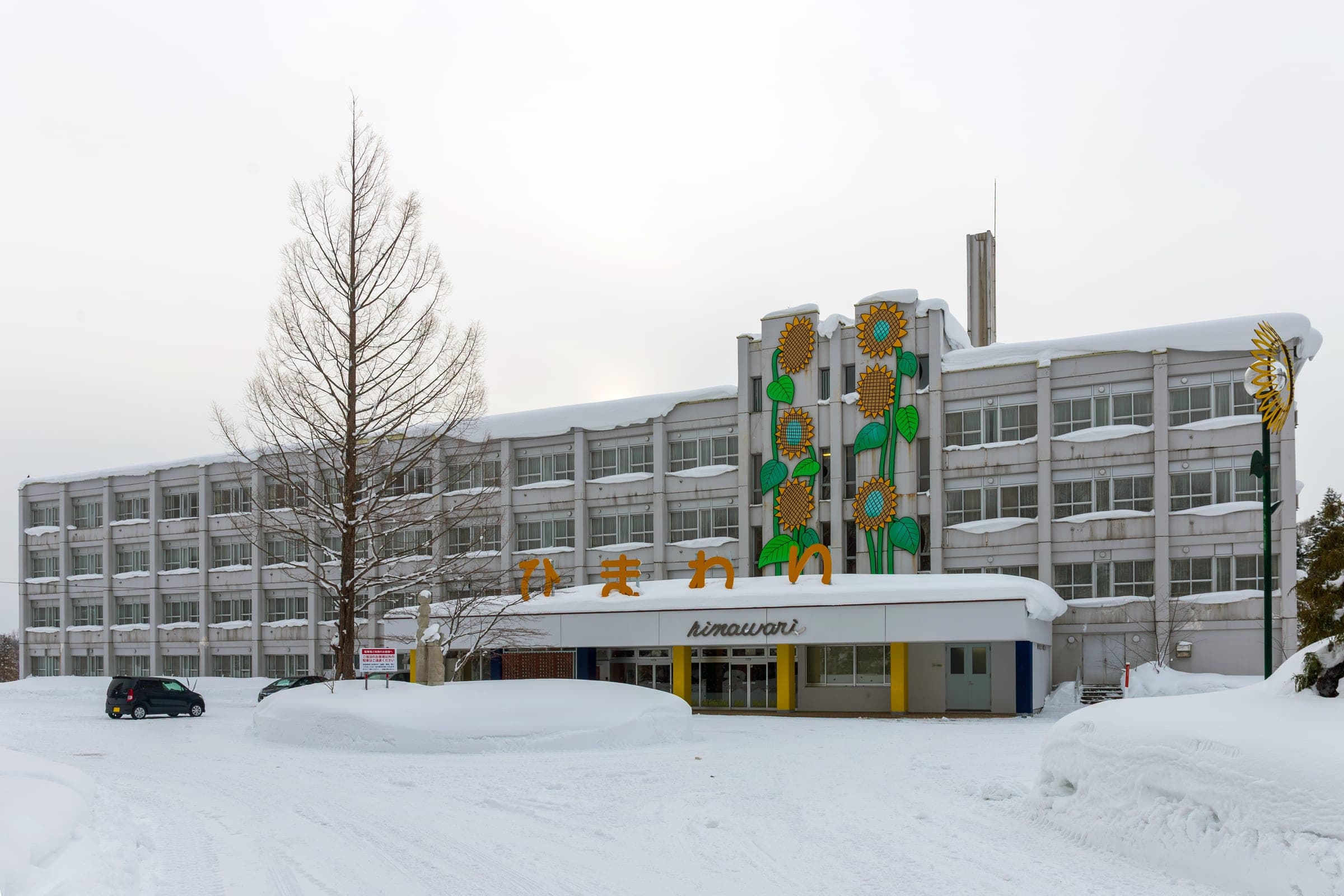 Hostel Himawari, a former high school in Yubari, stands behind deep snow under a blue sky