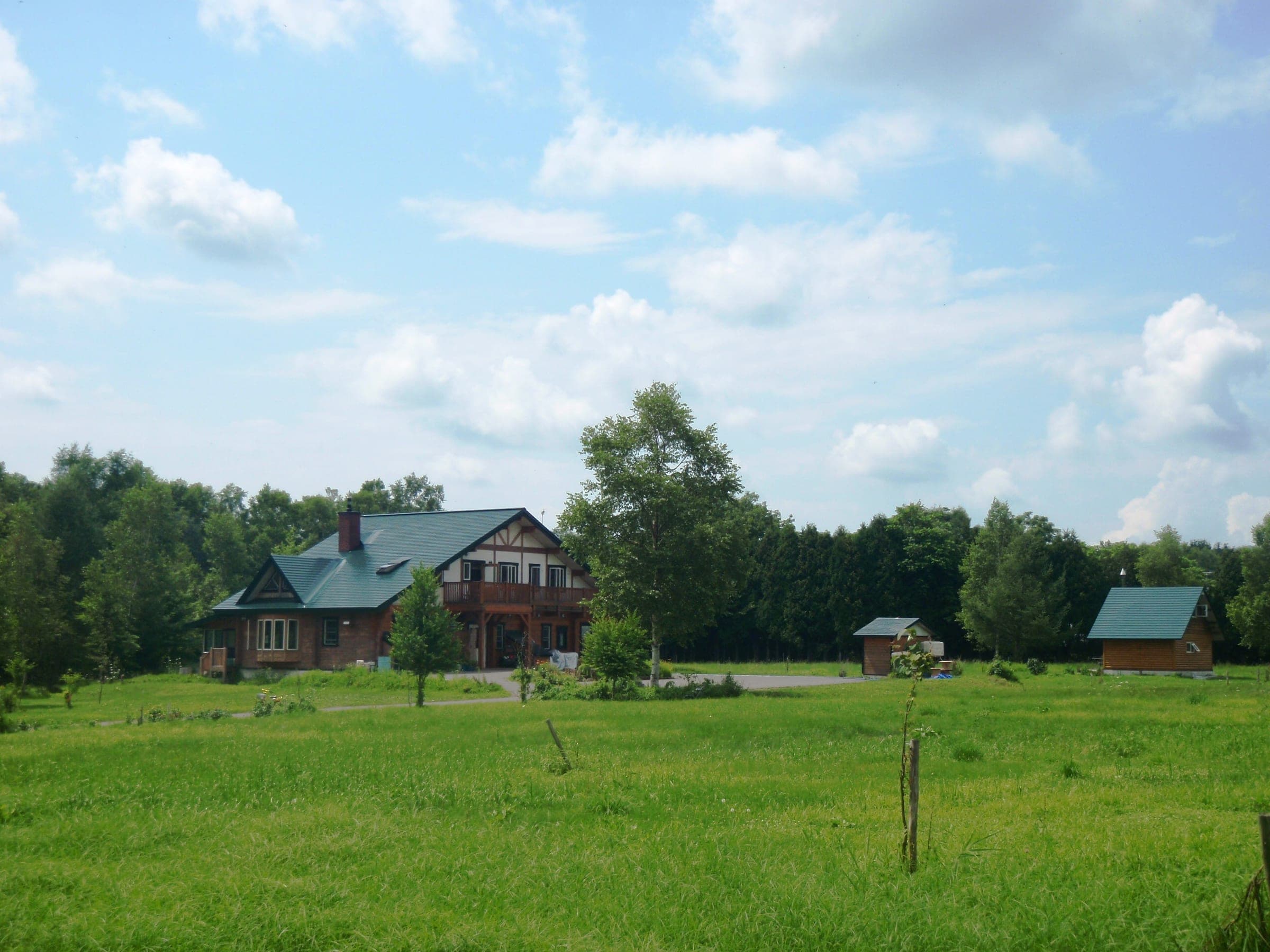 Timber buildings of the Yubari Forest hostel sit in a green meadow below wooded hills